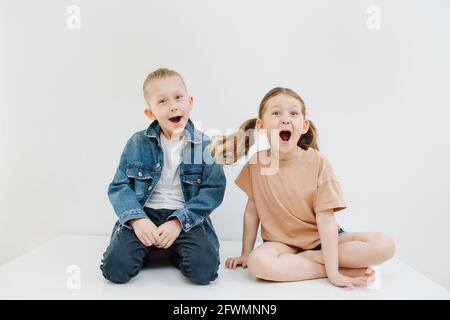 Lustige kleine Geschwister sitzen auf dem Tisch, grimazing, Öffnung Mund, gefälschte Überraschung Stockfoto