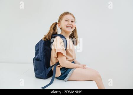 Schülerin sitzt auf dem Tisch und lächelt so weit sie kann. Weißer Hintergrund Stockfoto