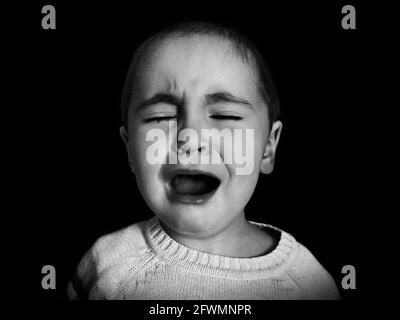 Ein einjähriges Mädchen mit kurzen Haaren weint unkontrolliert in Monochrom. Konzept der Angst, Depression, Kinderprobleme, Emotionen. Stockfoto