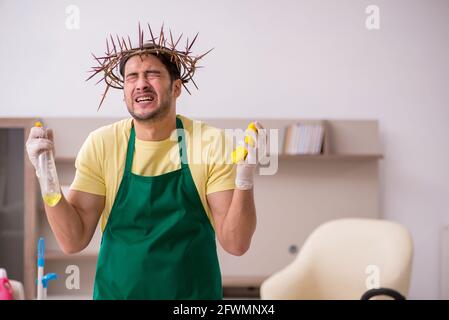 Junger männlicher Auftragnehmer, der auf dem Kopf einen stacheligen Kranz trägt und Hausarbeit leistet Stockfoto