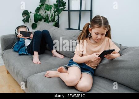 Beschäftigte kleine Geschwister, die ihre Freizeit damit verbringen, ihre Telefone zu beobachten Auf einer Couch Stockfoto