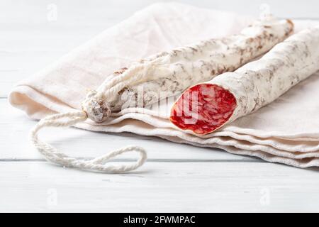 Zwei dünne katalanische Fuetwürste auf einem weißen Leinentuch über einem Holztisch. Nahaufnahme der traditionellen spanischen, trocken gehäuteten Schweinesalami mit weißem Edelschimmel Stockfoto