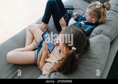 Zwei kleine Geschwister, die auf der Couch sitzen und Telefone nebeneinander beobachten Stockfoto