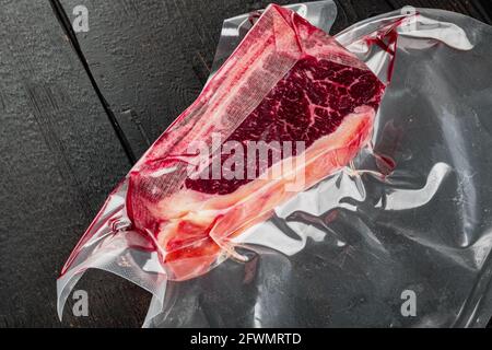 Frisches, riesiges und appetitliches Clubsteak im Vakuumverpackungsset auf schwarzem Holztisch-Hintergrund Stockfoto