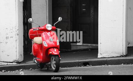 Ein leuchtend roter Vespa Roller Moped in einer Stadtstraße auf der Seite eines Hügels geparkt. Graffiti im Hintergrund. Stockfoto