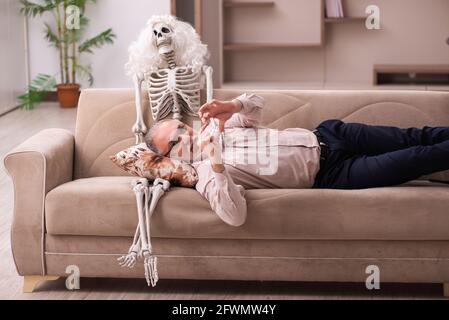 Alter Mann sitzt auf dem Sofa mit dem weiblichen Skelett In unsterbst Liebe Konzept Stockfoto