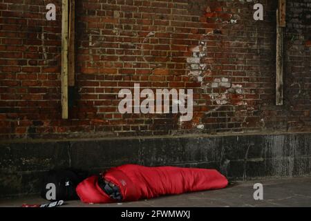 London (UK), 23. Mai 2021: Eine obdachlose Person wird unter einer Brücke gesehen, die in einem roten Schlafsack in der Nähe der Embankment-Station am Südufer schläft. Stockfoto