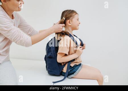 Mutter hilft ihrer Tochter, sich für die Schule vorzubereiten. Auf weißem Hintergrund. Stockfoto