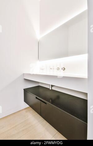 Luxuriöses Badezimmer-Design mit leuchtendem Spiegel über dem großen Waschbecken Schwarzer Schrank in der Wohnung Stockfoto