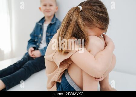 Schmollendes kleines Mädchen, das auf einem Tisch sitzt. Ihr Bruder beobachtete sie nervös. Stockfoto