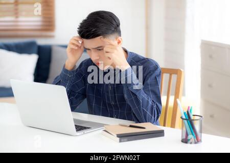 Junge asiatische Geschäftsmann Kopfschmerzen während der Arbeit auf Laptop-Computer mit Frist auf dem Schreibtisch zu Hause, Geschäftsmann mit Ausfall erschöpft und müde, stres Stockfoto