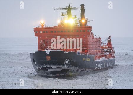 Sabetta, Region Tjumen, Russland - 4. April 2021: Der 50 ließ Pobedy Eisbrecher zieht in Eis. Bewölkt, leichter Schnee fällt. Stockfoto