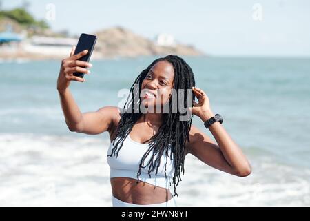 Schöne junge, frauige Frau, die an der Küste steht und nimmt Selfie nach dem Training Stockfoto