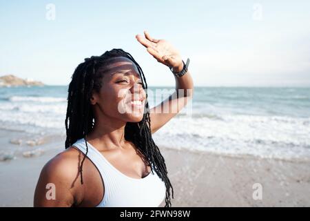 Fröhliche junge Frau, die ihre Augen mit Händen von Bright bedeckt Sonnenlicht beim Blick auf die Meereslandschaft Stockfoto