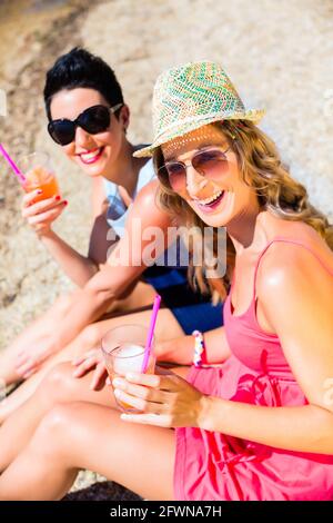 Frauen trinken Cocktails am Strand am Badesee in Sand Stockfoto