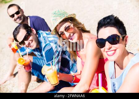 Vier Freunde sitzen auf See Strand mit Cocktails im Sommer Sonne Stockfoto