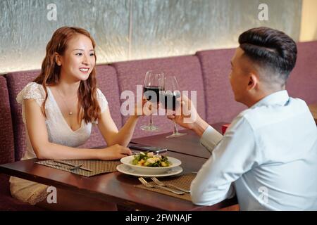 Fröhliches junges Paar, das beim romantischen Genuss mit Weingläsern toaste Datum in einem schönen Restaurant Stockfoto
