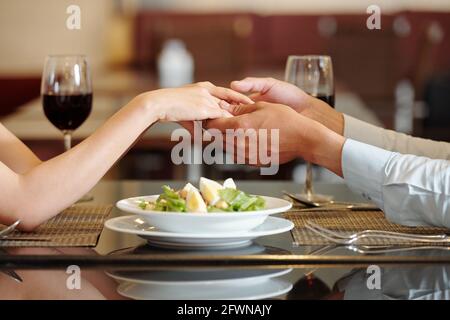 Nahaufnahme eines jungen Paares, das die Hände über den Teller hält Salat auf dem Restauranttisch Stockfoto