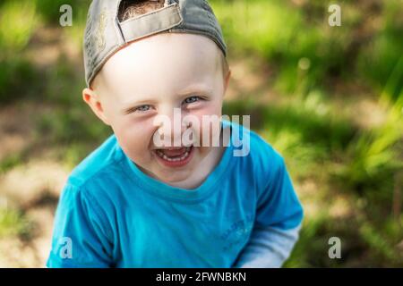 Frohe Kindheit. Lachender kaukasischer Junge mit Baseballmütze und Blick in die Kamera. Nahaufnahme. Stockfoto