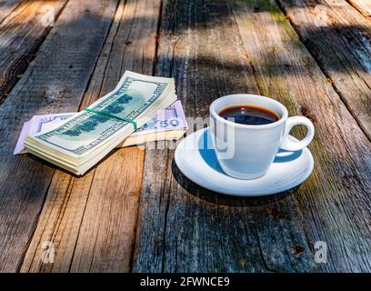 Eine Tasse Kaffee und ein Geldbündel auf einem Holztisch. Stockfoto