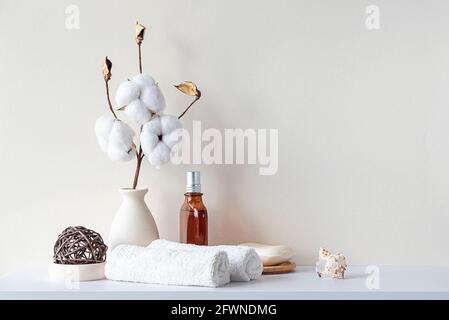 Badezimmereinrichtung in beigefarbenen Pastelltönen. Weißes Regal im Badezimmer mit Handtüchern, Seife, Parfüm-Flasche, Baumwollpflanze. Modell mit Platz für Text. Minimale c Stockfoto