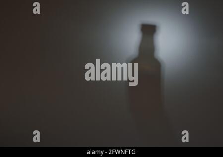 Flasche im Licht. Die verschwommene Silhouette einer Whiskey-Flasche. Unschärfter Schatten mit Rauschen. Abstrakter Hintergrund. Stockfoto