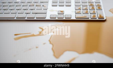 Verschüttete Tropfen schwarzen Kaffees auf einer weißen Computertastatur Stockfoto