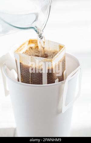 Kaffee mit Tropfkaffeesack in einer weißen Papiertasse zubereiten. Tropfenden Brühkaffee. Stockfoto