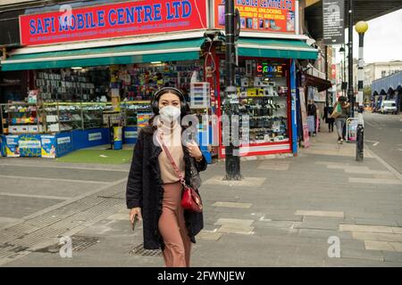 London, Brixton: Eine Frau, die eine Covid 19 Gesichtsmaske trägt, während sie auf einer Einkaufsstraße in Brixton spazieren geht Stockfoto