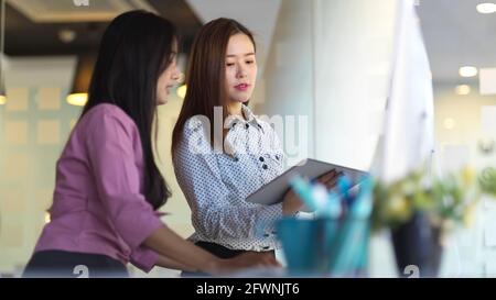 Seitenansicht von zwei Arbeiterinnen, die sich bei ihrem Projekt beraten In einem modernen Bürozimmer Stockfoto