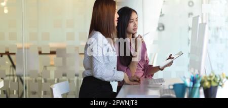 Seitenansicht von zwei Arbeiterinnen, die sich bei ihrem Projekt beraten In einem modernen Tagungsraum Stockfoto