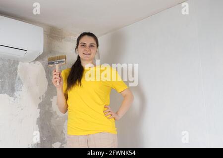 Eine Reparaturfrau klebt weiße Tapeten an der Wand in der Nähe Die Klimaanlage unter der Decke Stockfoto