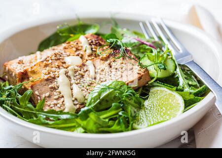 Brocken gebratener Tofu mit grünem Salat in einer weißen Schüssel. Asiatische Küche, veganes Food-Konzept. Stockfoto
