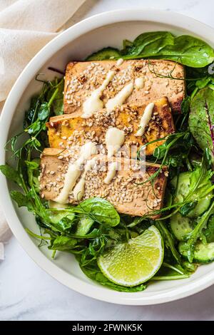 Gebratener Tofu mit grünem Salat und Nussdressing in einer weißen Schüssel. Asiatische Küche, veganes Food-Konzept. Stockfoto