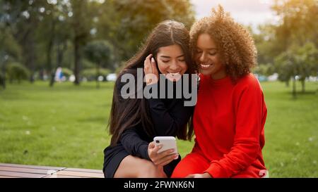 Diversity und Weiblichkeit Konzept. Glücklich lächelnd zuversichtlich junge gemischte Rennen Frauen sitzen Bank Park im Freien asiatische und afroamerikanische Frau ruht auf Stockfoto