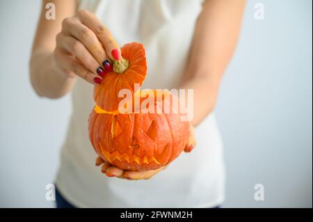 Weibliche Hände halten einen Kürbis für Halloween. Nahaufnahme einer Frau öffnet die Jack-o'-Laterne Abdeckung auf einem weißen Hintergrund am Vorabend aller Heiligen Stockfoto
