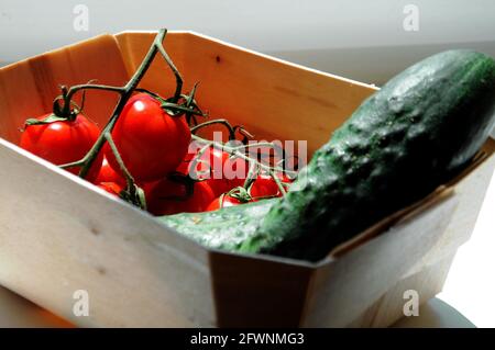 Grüne Gurken und rote Mini-Kirschtomaten in einem Holz Box nach dem Einkaufen auf dem lokalen Markt auf dem weißen Hintergrund Stockfoto