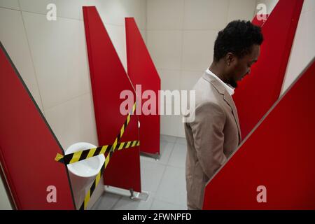 Grafikbild eines afroamerikanischen Geschäftsmannes, der öffentliche Toilette mit abgeklebtem Stall für soziale Distanzierung und covid Sicherheitsmaßnahmen benutzt, Kopierraum Stockfoto