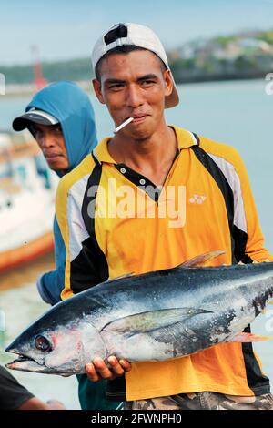 Der rauchende Fischer posiert mit einem Yellowfin-Thunfisch im geschäftigen Fischerhafen in diesem Ferienort im äußersten Süden: Tanjung Bira, Süd-Sulawesi, Indonesien Stockfoto