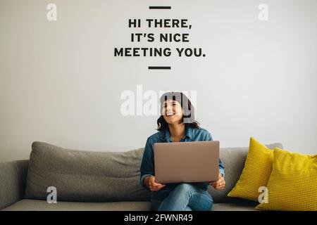 Frau, die einen Laptop in der Hand hielt und in der Lobby saß, schaute weg. Lächelnde Geschäftsfrau mit Laptop, der wegschaut und auf dem Sofa sitzt. Stockfoto