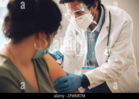 Medizinische Fachkraft, die Frau zu Hause impft. Arzt mit persönlicher Schutzausrüstung, der einer Frau eine Coronavirus-Impfung verabreicht. Stockfoto