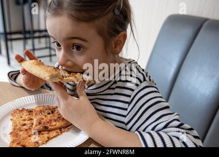 Ein süßes kleines Mädchen isst appetitlich ein Stück Pizza zum Mittagessen. Stockfoto