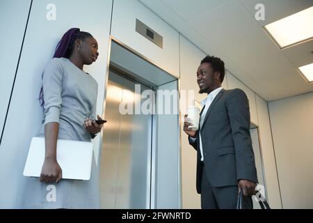 Blick aus der Perspektive auf zwei afroamerikanische Geschäftsleute, die darauf warten Fahrstuhl im Bürogebäude und Chat Stockfoto