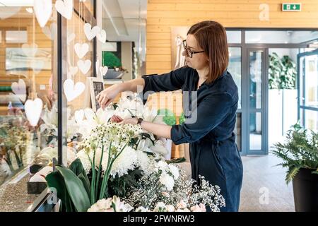 Junge Frau Floristin kümmert sich um Blumen in ihrem Geschäft. Small Business-Konzept, Blumenladen. Lieblingsarbeit. Seitenansicht. Stockfoto