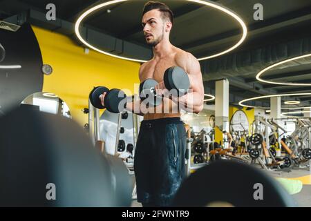 Hübscher junger sportlicher Bodybuilder, der Langhantel im Fitnessstudio macht Stockfoto