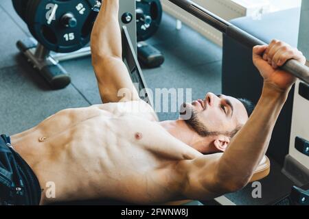 Ein sportlicher Mann, der eine Langhantelübung macht. Der professionelle Bodybuilder macht mit einer Langhantel ein Bankdrücken-Workout Stockfoto