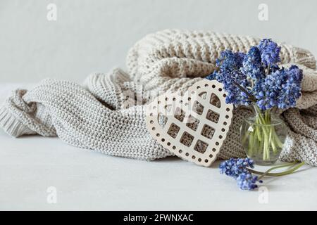 Warme Strickpullover in Pastellfarben, ein Bouquet aus Muscari-Blumen und ein dekoratives Holzherz. Stockfoto