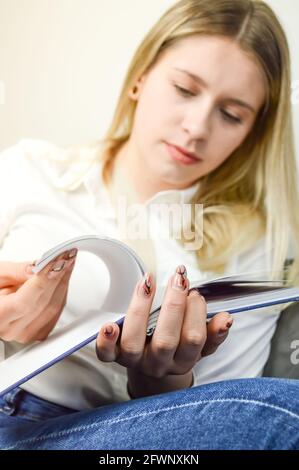 Schöne junge blonde Frau, die schnell durch die Seiten eines Buches blättert, sich auf die Hände und das Buch konzentriert Stockfoto