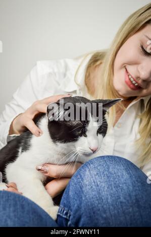 Schöne junge blonde Frau kuscheln ein gelangweilt jung schwarz und Weiße Katze aus der Nähe Stockfoto