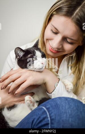 Schöne junge blonde Frau kuscheln ein gelangweilt jung schwarz und Weiße Katze aus der Nähe Stockfoto